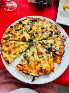 Sliced Cheese Pizza Topped with Black Olives and Vegetables on a White Plate over a Red Tablecloth, Bubbly and Browned Cheese Edges Present.
