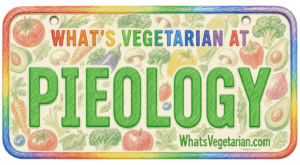 Colorful rectangular sign with a rainbow border reading 'WHAT'S VEGETARIAN AT' and a large word 'PIEOLOGY' surrounded by vegetables; includes 'WhatsVegetarian.com'