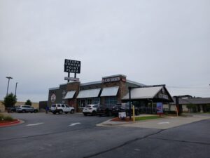 Exterior of Slim Chickens restaurant at Ozark Center Point Place with a row of parked cars in front on a cloudy day